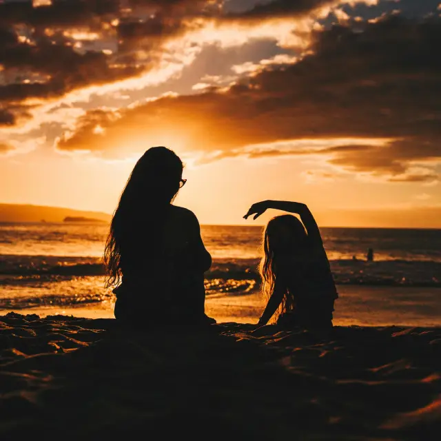 Mamma och dotter sitter på en strand vid solnedgången